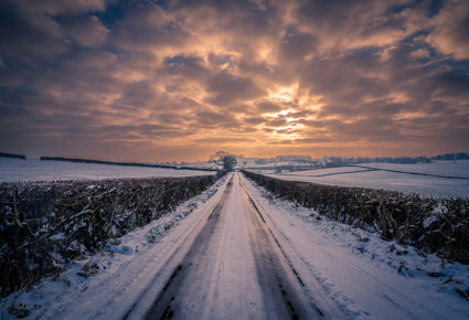 Road covered in snow, surrounded by fields that are also covered in snow