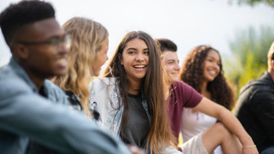 Group of five young people sitting outdoorsk, with the focus is on a brown-haired person in the centre.