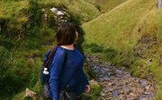 Woman admiring green hills while standing next to a dry river creek.