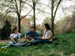 Three students sit in a park and chat.