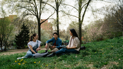Three students sit in a park and chat