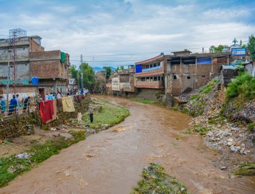 An overflowig river running through the heart of an urban area in Pakistan. The water is tinged brown with mud,