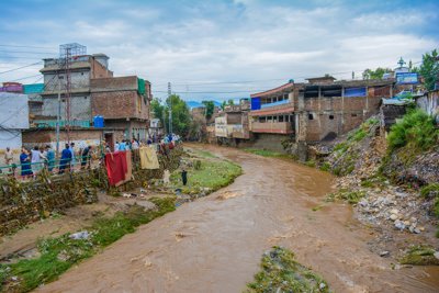 An overflowig river running through the heart of an urban area in Pakistan. The water is tinged brown with mud,