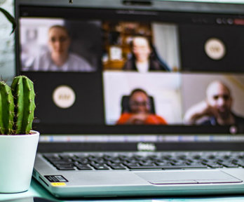 A cactus, mobile phone, laptop showing open conference call, and blue pen.