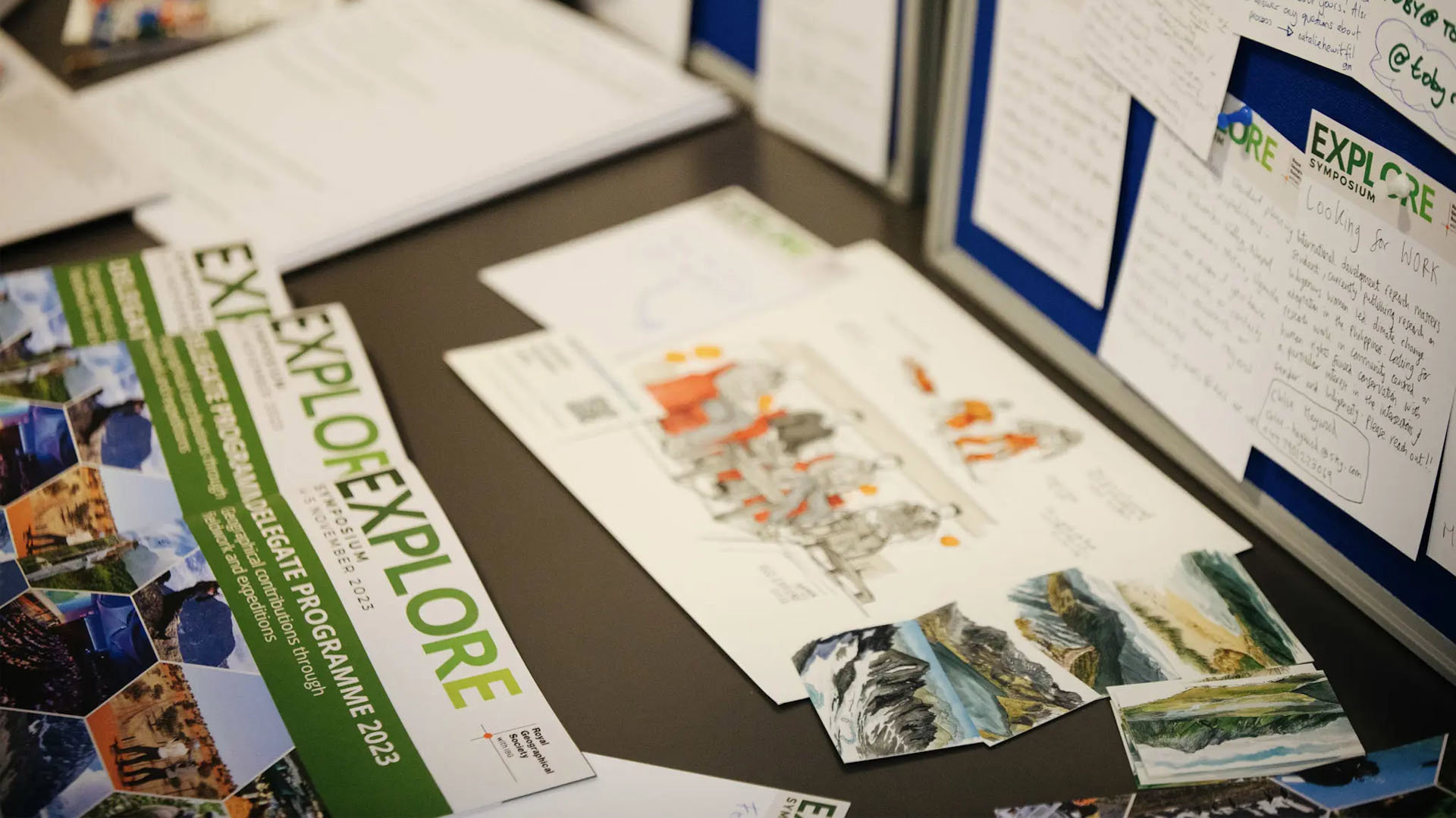 Tabletop full of images of mountains and leaflets from the Society's Explore symposium 2023. One of the leaflets reads Delegates programme 2023.