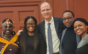Five people dressed in formal attire smiling for picture.