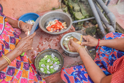 Cooking pots containing a variety of vegetables and two women cutting items