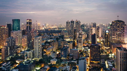 A cityscape at dusk with modern high rise buildings and lit up streets.