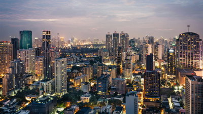 A cityscape at dusk with modern high rise buildings and lit up streets. 