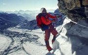 A man in climbing gear on a snowy rock buttress.