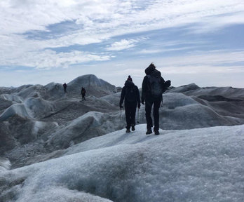 Four people walking across an undulating glacial landscape carrying equipment.