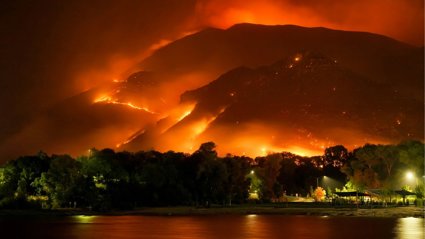 Bay at night with behind it mountains that are on fire.