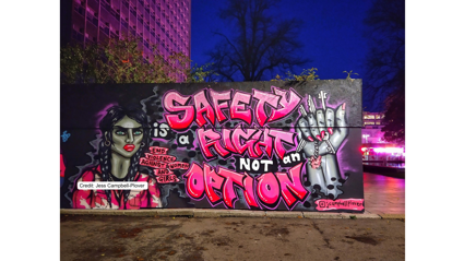 Graffiti mural with bold pink letters stating 'Safety is a right, not an option' alongside a message against violence toward women.