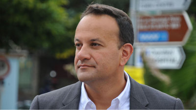 Headshot of Leo Varadkar wearing grey suit against backdrop of street signs.