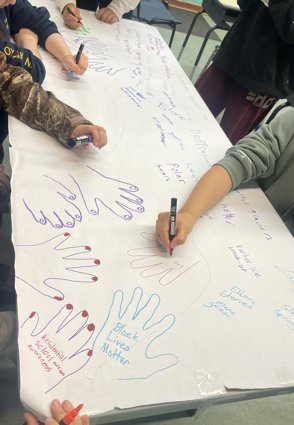 Five children draw hand prints on a large piece of white paper on which they also write words including black lives matter, polar bears and depression.