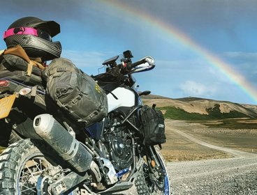 Motorbike on gravel road with a rainbow in the sky.