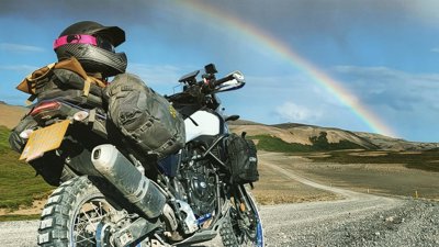 Motorbike on gravel road with a rainbow in the sky.