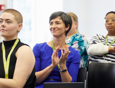 Three conference delegates listening to a presentation and apploading.