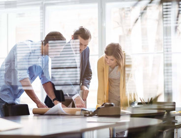 Three professionals leaning over a table looking at plans.