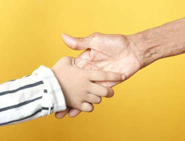 Two hands reaching out to hold each other on yellow background.