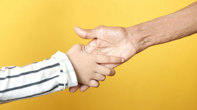 Two hands reaching out to hold each other on yellow background.