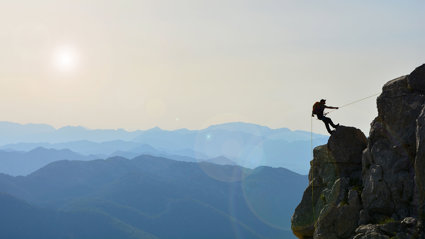 A lonely mountaineer climbing a mountain top, against a backdrop of a vast mountain range.