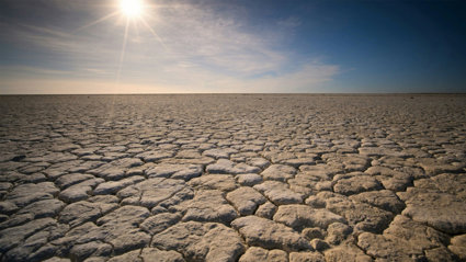 Dry, flat landscape with cracked land caused by drought. The sun is shining fiercly above the dry earth.