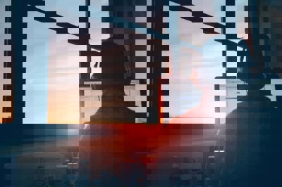 Person using a computer wearing headphones with a sunset coming through thew window