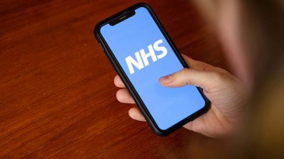 Person holding a phone with NHS logo in white with blue background.