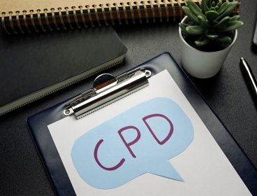 Clipboard with the letters 'CPD' written on paper, surrounded by office stationary.