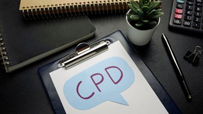 Clipboard with the letters 'CPD' written on paper, surrounded by office stationary.