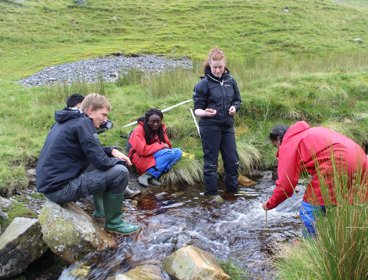 Group of pupils undertaking river fieldwork in a small stream.