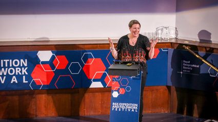 Speaker smiling while giving a lecture behind a lectern that says RGS expedition and fieldwork festival.