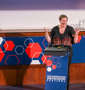 Speaker smiling while giving a lecture behind a lectern that says RGS expedition and fieldwork festival.