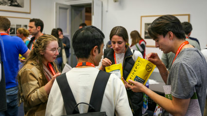 Four people at a conference standing in a circle. The two on the right each hold a bag that says 'firedepot'. The two on the left are watching them open the bags.