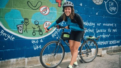 Franke Dewar next to bike pointing at wall mural about the environment
