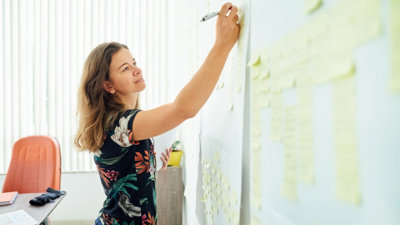 Person writing on a post-it note stuck on a wall.
