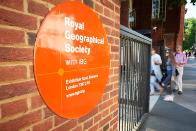 Sign on the outside of the Society's building close to the entrance, with three people walking in.