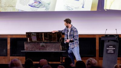 Person on stage opening large old chest.