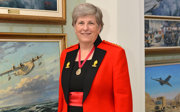 A woman in ceremonial military attire posing in front of several paintings that all have jets depicted on them.
