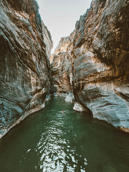 Gorge rocks with green river running through and person swimming
