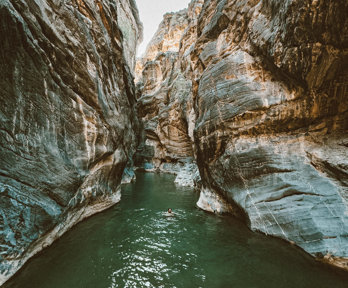 Gorge rocks with green river running through and person swimming