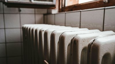 A close up of a white metal radiator underneath a window during the day.