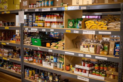 Rice, pasta, and various other tin foods are stacked on a metal shelf cushioned with wooden board.
