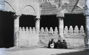 Black and white photograph showing three people sitting in a courtyard.
