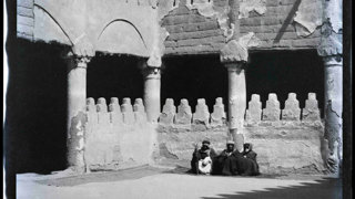 Black and white photograph showing three people sitting in a courtyard.