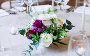 A close-up of a purple, white and green floral arrangement surrounded by candles on a formal dinner table.