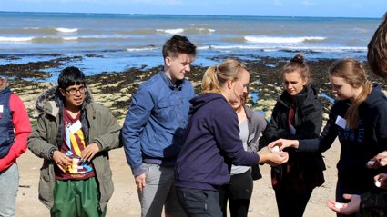 Six secondary school pupils standing on a beach inspecting pebbles.