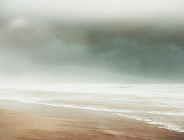 Empty beach with waves under a dark, cloudy sky.
