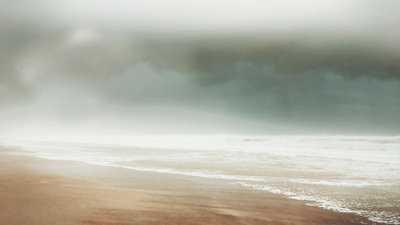 Empty beach with waves under a dark, cloudy sky.